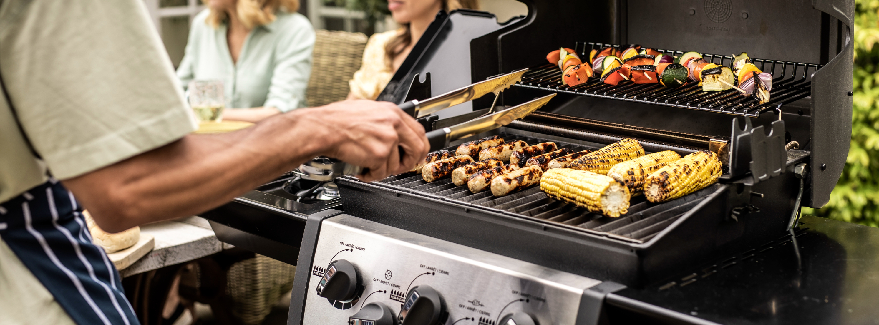 Man cooking sausages and sweetcorn on his gas bbq